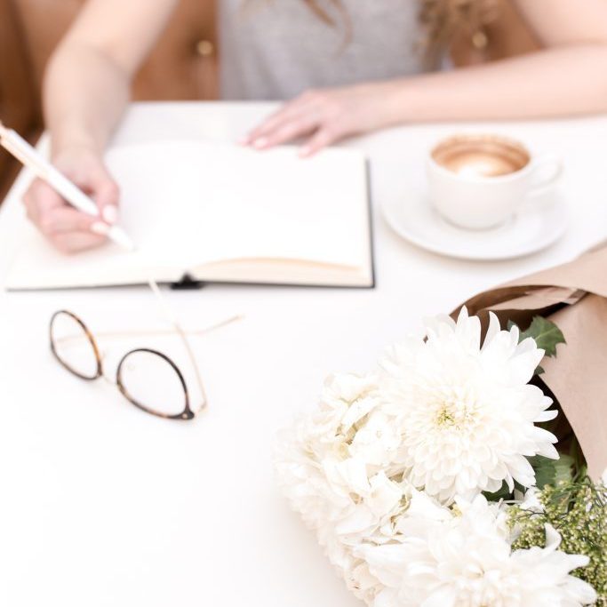 Girl writing in pad, glasses and bunch of flowers