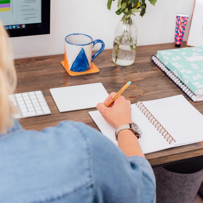 Woman sitting at desk writing in a note pad.