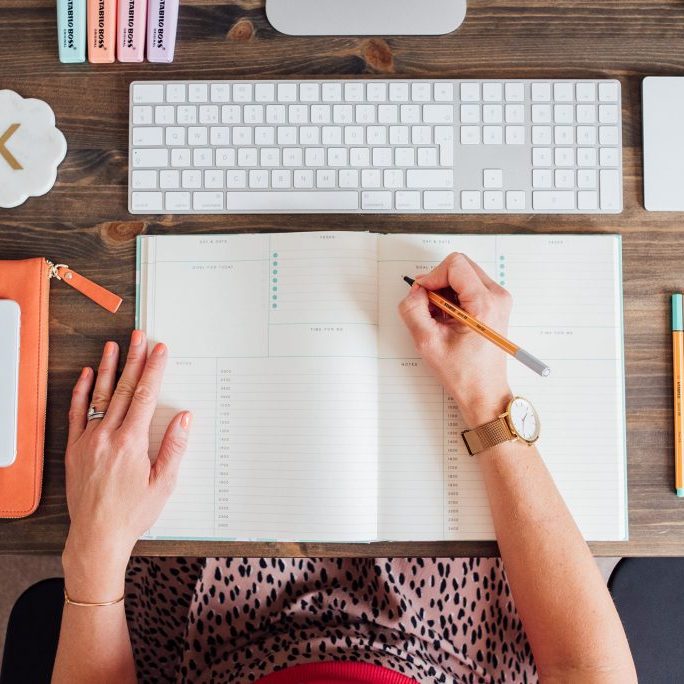 Virtual Assistant writing in a daily planner to reduce overwhelm